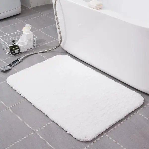 Weisse Badematte flauschig im Badezimmer, weicher Teppich vor Badewanne.