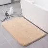 Beige Badteppich mit weichem Flor vor der Badewanne auf grauem Fliesenboden.