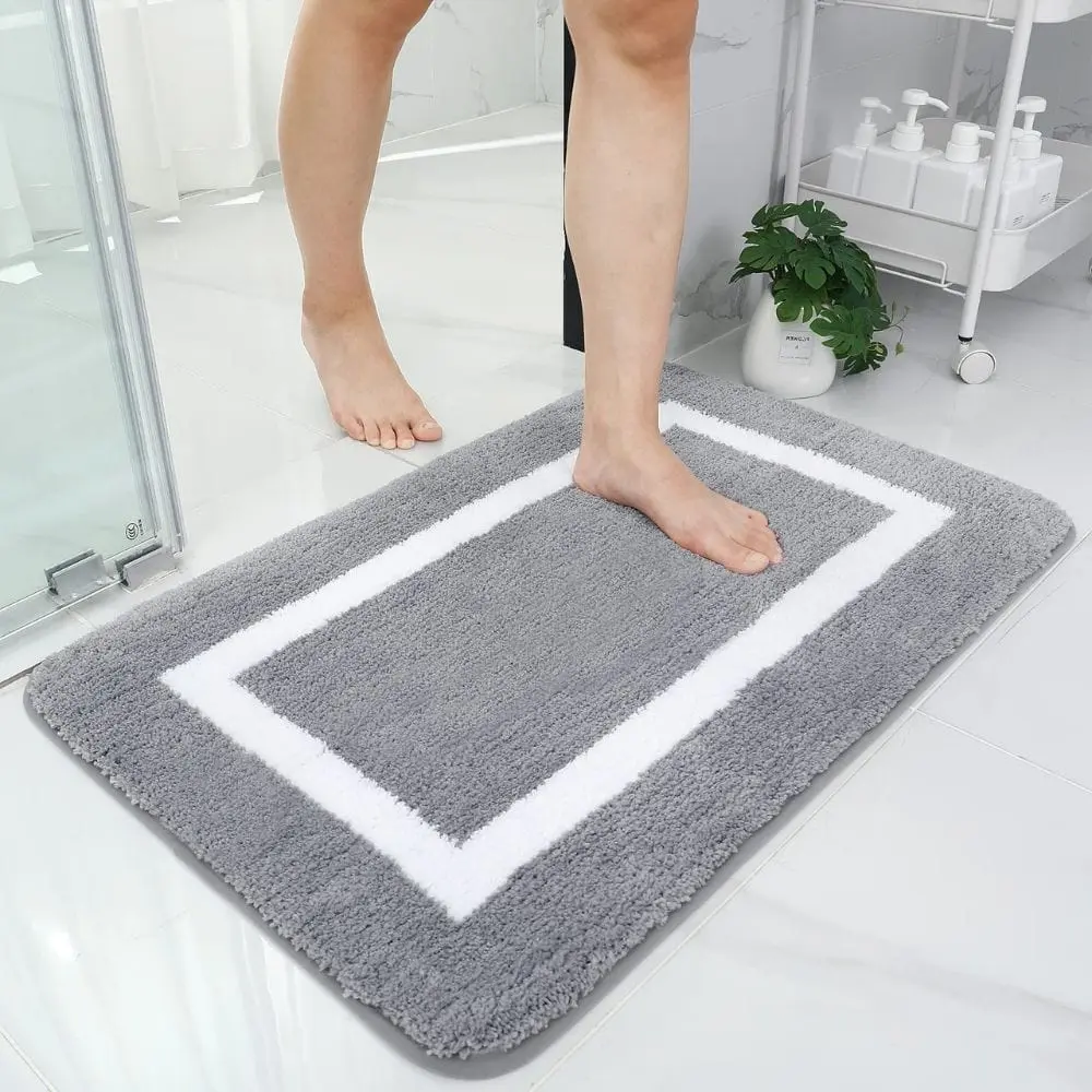 Grosse Badematte grau mit weissem Rand, weiches Material, ideal für Badezimmer.