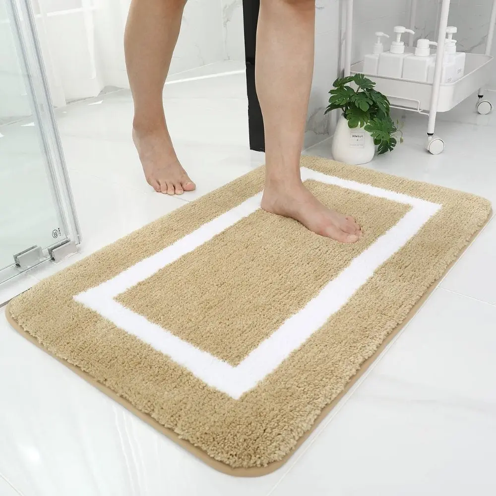 Grosse Badematte beige mit weißem Rand, weiches Material, ideal für Badezimmer.