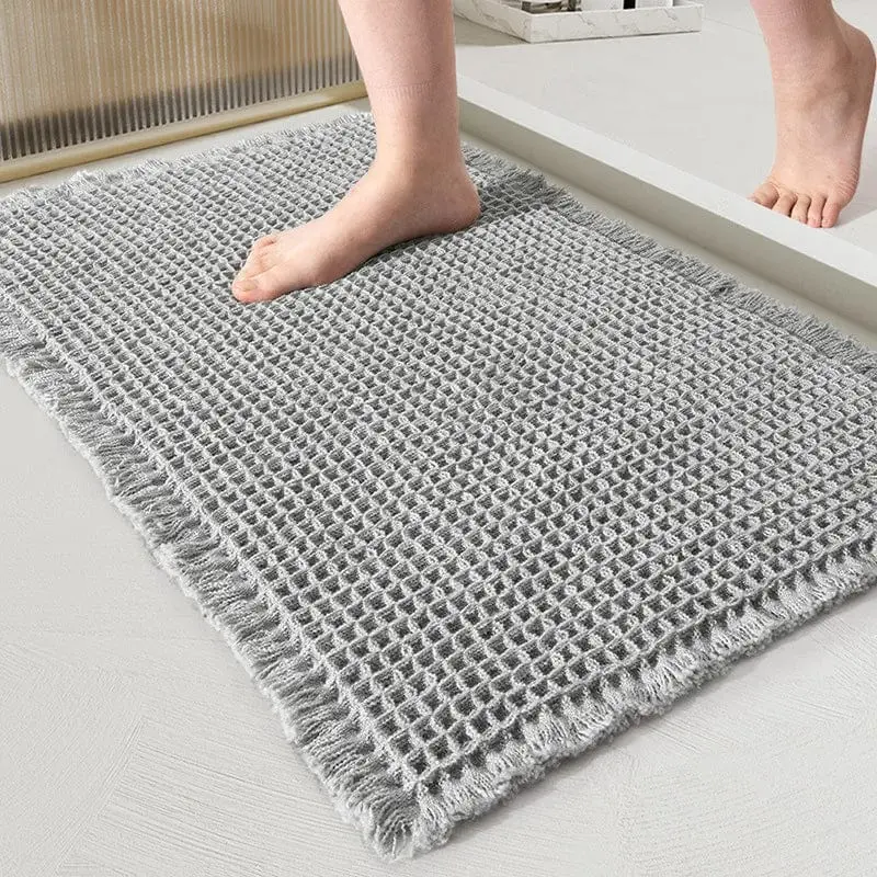 Grauer, umgefalteter Badteppich mit Fransen und Struktur, ideal fürs Badezimmer.